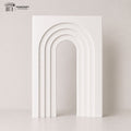 Modern white layered arch backdrop standing in a minimalist studio setting with soft neutral tones and elegant curved design for party and event decor.
